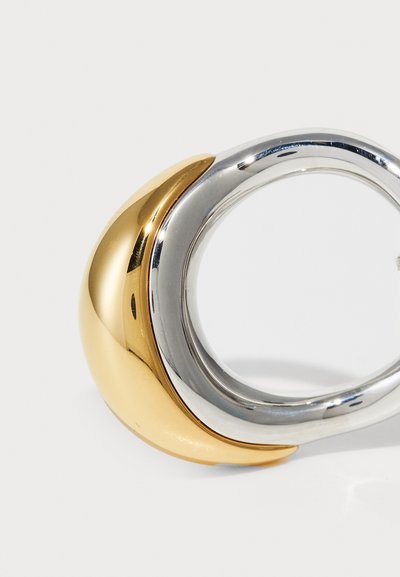 Zlatý a strieborný kovový prsteň so hladkým, zaobleným dizajnom. Má rozdelený vzhľad, kombinuje leštené zlaté a strieborné povrchy.