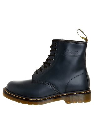 Czarny skórzany botek Dr. Martens za kostkę z ośmioma oczkami, widocznym żółtym przeszyciem, podeszwą z poduszką powietrzną i oznaczoną pętelką na pięcie.