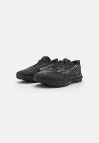 Des chaussures de trail running noires avec une tige texturée, des accents réfléchissants et des semelles en caoutchouc épaisses. Présente le logo "GORE-TEX" sur le côté.