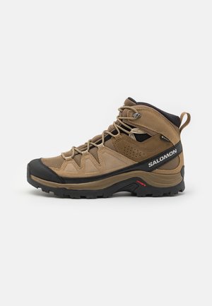 Bottes de randonnée montantes marron et noires avec semelle robuste, fermeture à lacets à l'avant, panneaux en mesh et en suède, avec marquage « Salomon » sur le côté.