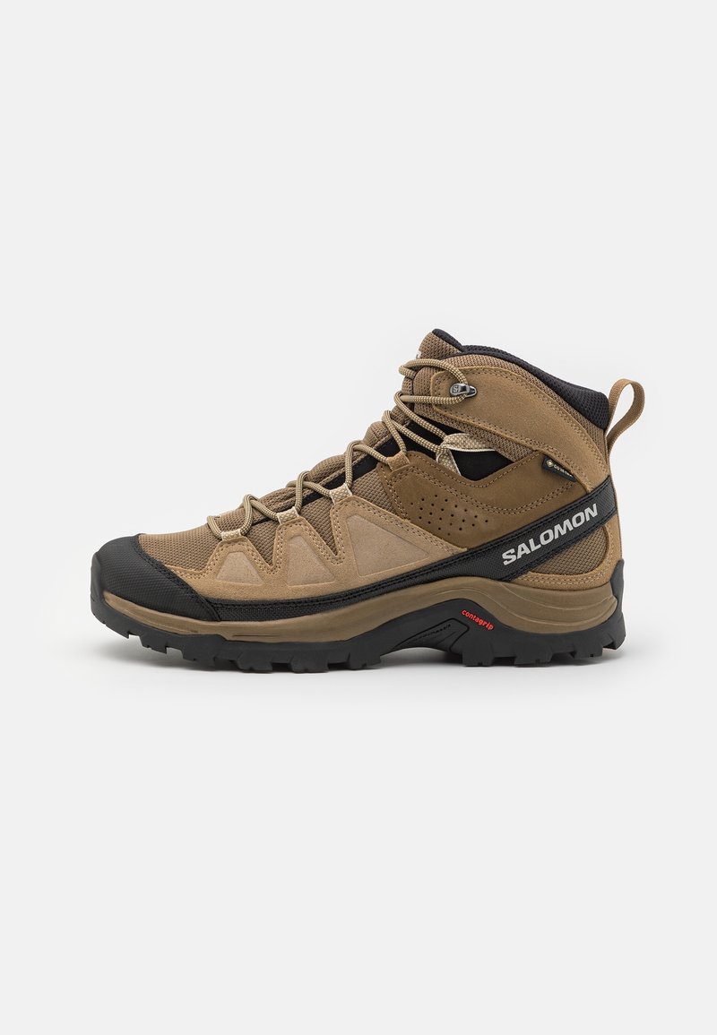 Bottes de randonnée montantes marron et noires avec semelle robuste, fermeture à lacets à l'avant, panneaux en mesh et en suède, avec marquage « Salomon » sur le côté.