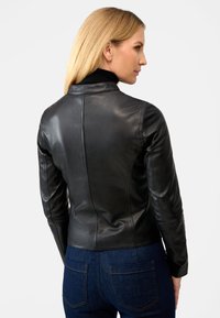Schwarze Lederjacke mit elegantem Design, featuring einen Stehkragen, figurbetonter Form und glatter Oberfläche, kombiniert mit blauen Jeans.