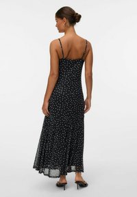Robe maxi noire à pois avec fines bretelles, corsage ajusté, ourlet évasé et superposition en tissu transparent. Accentuée de pois bleu clair.