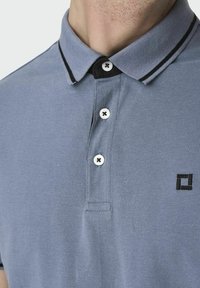 Camisa polo en mezcla de algodón azul claro, con un collar negro ribeteado, tres botones blancos y un logotipo negro bordado.
