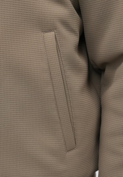 Καφέ σακάκι με υφή και διακριτό σχέδιο βάφλας, διαθέτει πλευρική τσέπη. Το ύφασμα έχει λεία επιφάνεια, που αναδεικνύει μια  μίξη ανθεκτικότητας και άνεσης.