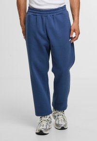 Marineblauwe sportbroeken met een elastische tailleband, een relaxte pasvorm en een gladde textuur, gecombineerd met zilveren sportschoenen.