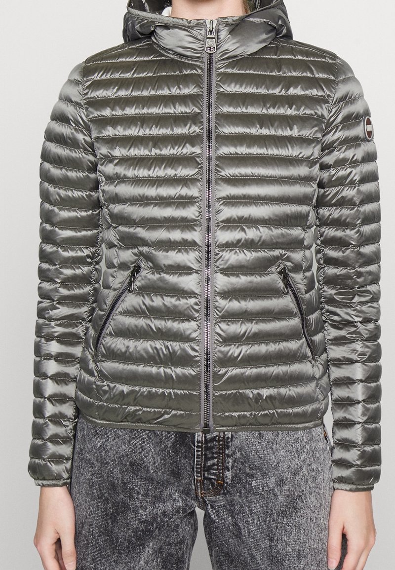 Padded gray jacket with ribbed texture, zip front, and hood. Features zippered pockets and elastic cuffs for warmth and comfort.