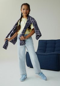 Tricou galben deschis purtat pe sub o cămașă violet în carouri, asortat cu blugi albaștri deschis și adidași asortati. Design simplu, croială lejeră.