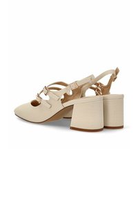 Zapatos de tacón en color beige con puntera afilada, que cuentan con un tacón ancho de textura de cocodrilo y correas de tobillo ajustables con detalles en tono dorado.