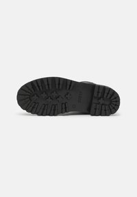 La semelle de botte en caoutchouc noir présente un motif de semelle robuste avec des rainures profondes, un logo en relief et une construction solide pour une durabilité accrue.