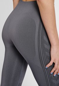 Szare legginsy o wysokim stanie z teksturowanym, prążkowanym wzorem oraz siateczkowymi panelami po bokach, zapewniającymi wentylację i podkreślającymi sylwetkę.