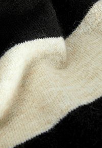 Strickstoff mit schwarzen und cremfarbenen Streifen. Weiche Textur mit einem Farbmix, der ein glattes Finish und feine Details präsentiert.