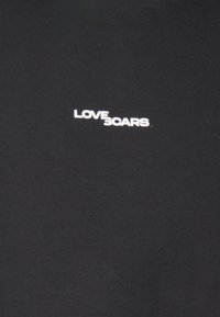 Černé bavlněné tričko s bílým potiskem textu "LOVE SCARS" na hrudi. Tkanina má hladkou texturu a volný střih.