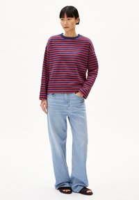 Gestreiftes langärmliges Shirt in Rot und Marineblau, kombiniert mit hellblauen, weiten Jeans. Hat einen Rundhalsausschnitt und einen lockeren Schnitt.