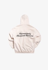 Sudadera crema con bolsillo canguro y capucha. Cuenta con texto en cursiva "Prendas Reconocidas Internacionalmente" en negro contrastante. Textura suave.