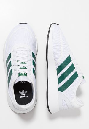 Hvide Adidas-sneakers med grønne striber, mesh-tekstur, snørebånd og sorte indlægssåler, vist fra top- og sidevinkler på en hvid baggrund.