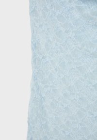 Tissu en dentelle bleu clair avec des motifs floraux et une texture de maille complexe, présenté en gros plan sur un fond neutre.