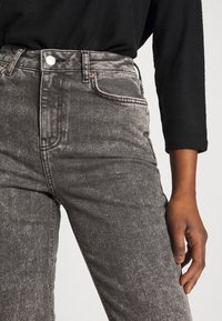 Jeans de mezclilla de tiro alto en negro con efecto lavado ácida, con costuras en contraste, bolsillos frontales y cierre de botón metálico.
