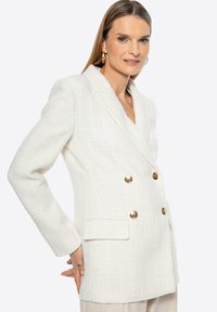 Blazer bianco doppiopetto realizzato in tessuto strutturato con bottoni dorati, presenta un colletto a rever e tasche frontali.