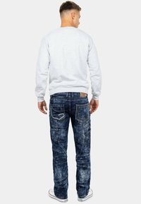 Jeans in denim blu sbiadito, a gamba dritta, con molteplici tasche e dettagli ricamati sul retro. Abbinati a una felpa grigia chiara.