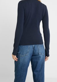 Námořnická halenka s dlouhým rukávem a slim fit, vyrobená z hladkého materiálu, kombinovaná s volnými světle modrými džínami s kapsami na zadní straně.
