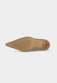 Semelle d'une chaussure à bout pointu avec une semelle en caoutchouc beige texturée et un talon en bois, marqué "ALDO" près de la zone de la voûte plantaire.