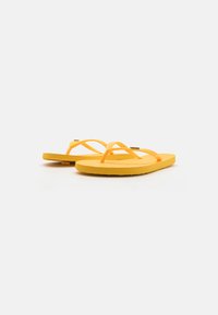 Gula flip-flops med platt gummisula och tunna, korsade remmar. Materialet är slätt, med en texturerad yta på sulan.