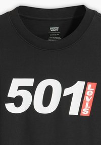 Juodas medvilnės marškinėliai su apvalia kaklo iškirpte ir grafiniu dizainu, kuriame baltais rašmenimis išspausdinta "501" ir raudonai "Levi's". Senovinis siluetas, glotni tekstūra.