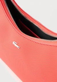 Koralfarvet pung lavet af tekstureret stof med en sølvfarvet lynlås og sort indre, med et lille hvidt logodetalje.