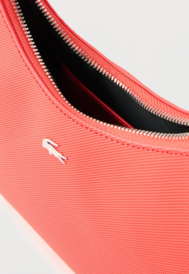 Koraalrode tasje gemaakt van tekstuurstof met een zilveren ritssluiting en een zwarte binnenkant, voorzien van een klein wit logodetail.