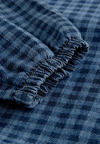 Trapani denim s tamnoplavim i svijetloplavim uzorkom pseće zube, s elastičnim rubom sa skupljenom teksturom i kontrastnim šavovima.