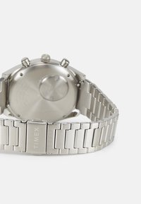 Silberne Armbanduhr aus Edelstahl mit einem segmentierten Armband, runder Gehäuseform, drei Tasten an der Seite und einer glatten Rückseite für ein poliertes Finish.
