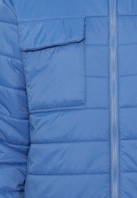 Blue puffer jacket with a zip front closure, horizontal quilted texture, and a flap pocket on the left chest. Soft synthetic material.