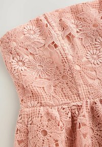 Rosa spetsklänning med blommönsterbroderi, intrikata utskärningar, figurnära midja och utsvängd kjol, tillverkad av lätt textil.