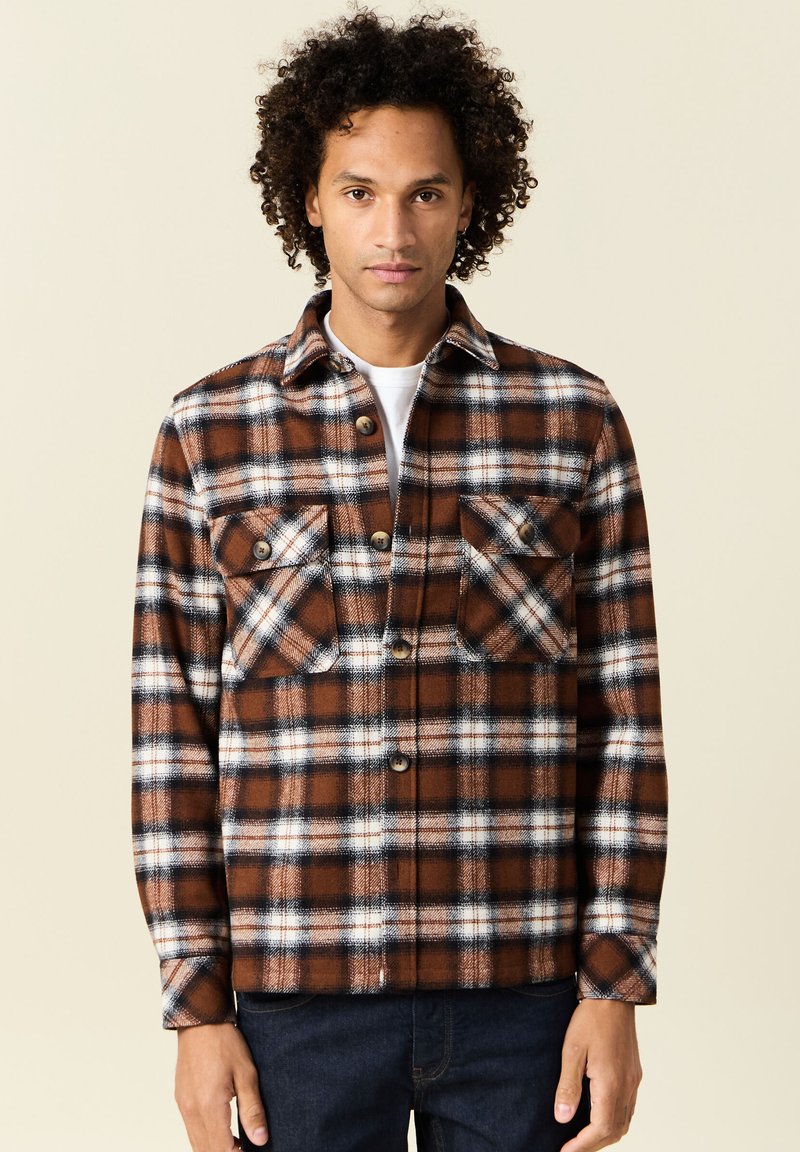 Giacca a camicia a quadri marrone e bianco in morbido tessuto, con due tasche sul petto, chiusura a bottoni e colletto.