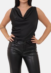 Sort ærmeløs top med en draperet halsudskæring, lavet af glat stof. Kombineret med slanke sorte bukser i kunstlæder med en tætsiddende pasform.