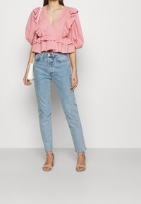 Růžová blůza s volány a hlubokým výstřihem ve tvaru V, kombinovaná se světle modrými džínami s vysokým pasem a světle růžovými sandály na podpatku. Minimalistická bílá kabelka.