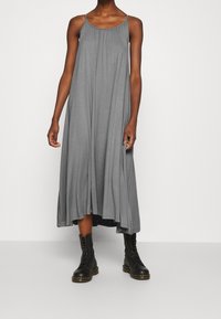 Grå, ärmlös maxiklänning med samlad detalj vid halsringningen; har en lös passform och faller till mitten av vaden, tillsammans med svarta snörboots.