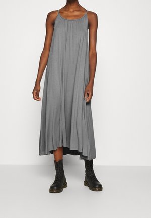 Robe maxi sans manches grise avec des détails froncés au niveau du décolleté ; elle a une coupe ample et arrive au milieu du mollet, associée à des bottes noires à lacets.