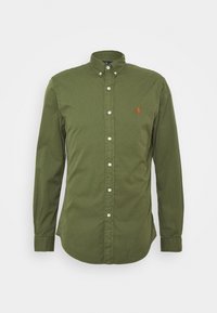 Grön långärmad skjorta i bomull, med en knappad krage, framknappar och en broderad logotyp i rött på bröstet.