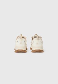 Zapatillas deportivas beige con parte superior texturizada, suela en contraste y suela de goma. Cuenta con una lengüeta en la parte posterior y detalles de marca mínimos.