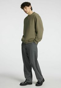 Olivgrön oversized sweatshirt med rund halsringning, kombinerad med grå vida byxor. Outiften kompletteras av svarta klumpiga skor.