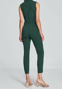 Grüner ärmelloser Jumpsuit mit tailliertem Design, schmal zulaufenden Beinen und definiertem Bund, kombiniert mit hautfarbenen Blockabsatzsandalen.