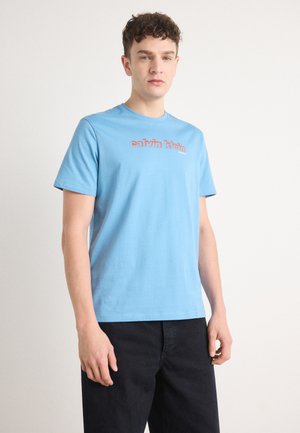 Lyseblå bomulds t-shirt med rund hals og korte ærmer. Har "calvin klein" logo i rød tværs over brystet. Ensfarvet, simpel design.