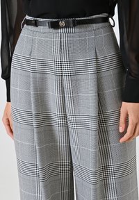 Plooibroek met hoge taille in een zwart-wit ruitpatroon, met een soepele stoftextuur en een contrasterende zwarte riem.