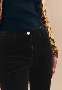 Sorte fløjlsjeans med en tætsiddende pasform, udstyret med en sølvfarvet knaplukning i taljen og forlommer. Tekstureret stof synligt.