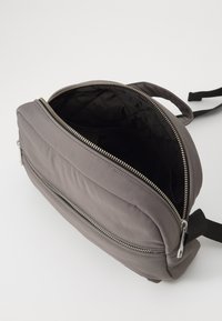 Zaino in poliestere grigio con interno imbottito, chiusura a doppia zip e tasca esterna con zip. Spallacci regolabili e texture del tessuto visibile.