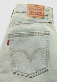 Τσέπη στο πίσω μέρος ανοιχτόχρωμου τζιν με το κόκκινο ταμπελάκι της Levi's και καφέ δερμάτινο σήμα Levi Strauss & Co. πάνω από τη μέση του παντελονιού.