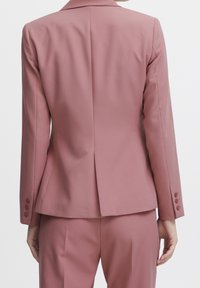 Vaaleanpunainen räätälöity pikkutakki, sileä kangas, jäsennellyt hartiat, yksittäinen takahalkio, viisi nappia kussakin hihansuussa, istuva malli.