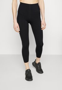 Schwarze hochtaillierte Leggings mit passgenauer Form, die über eine glatte Textur und einen knielangen Schnitt verfügen und mit schwarzen Sportschuhen kombiniert sind.